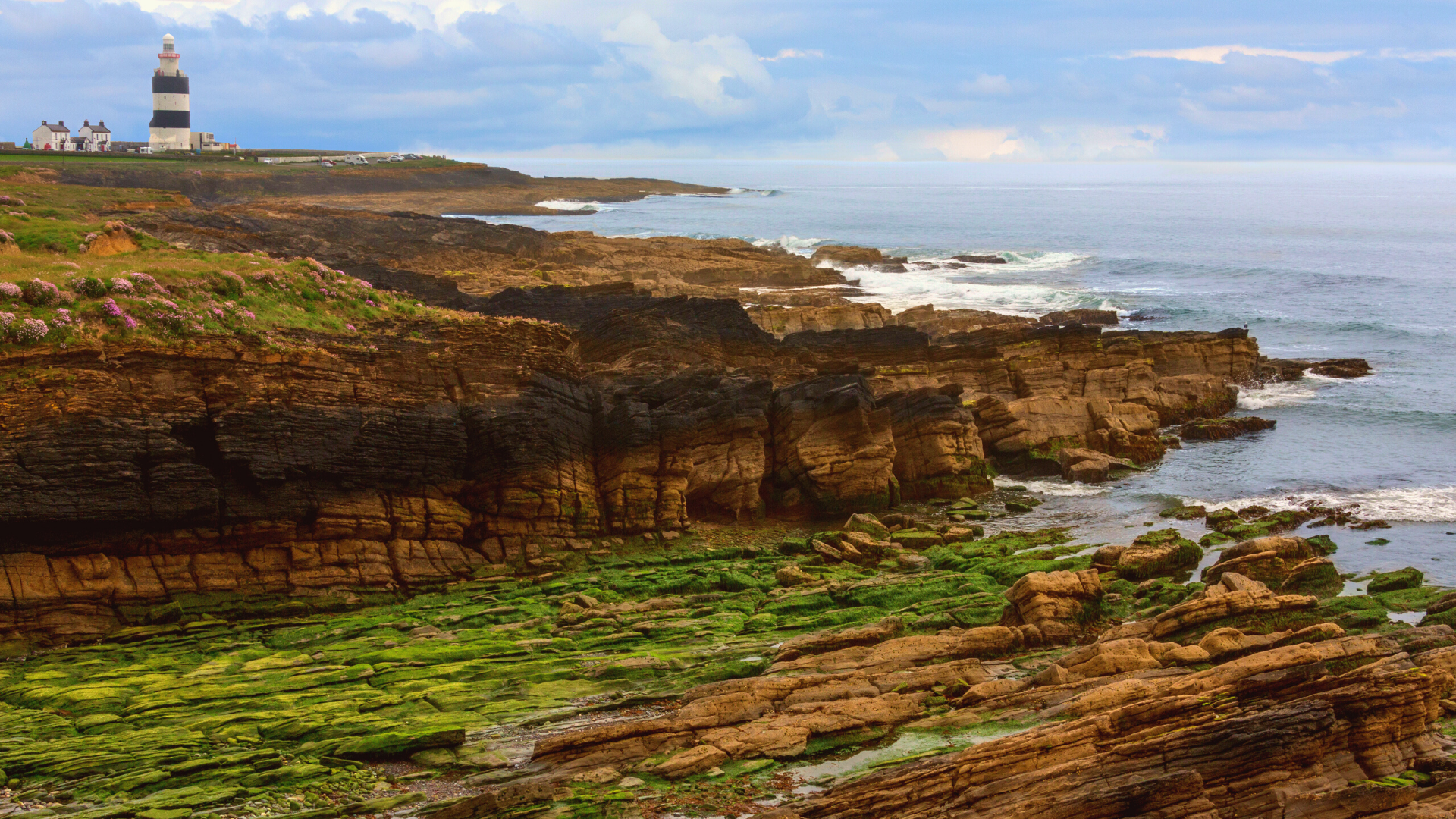 Coastal view of Clonganny House with rugged cliffs and lighthouse in the background.