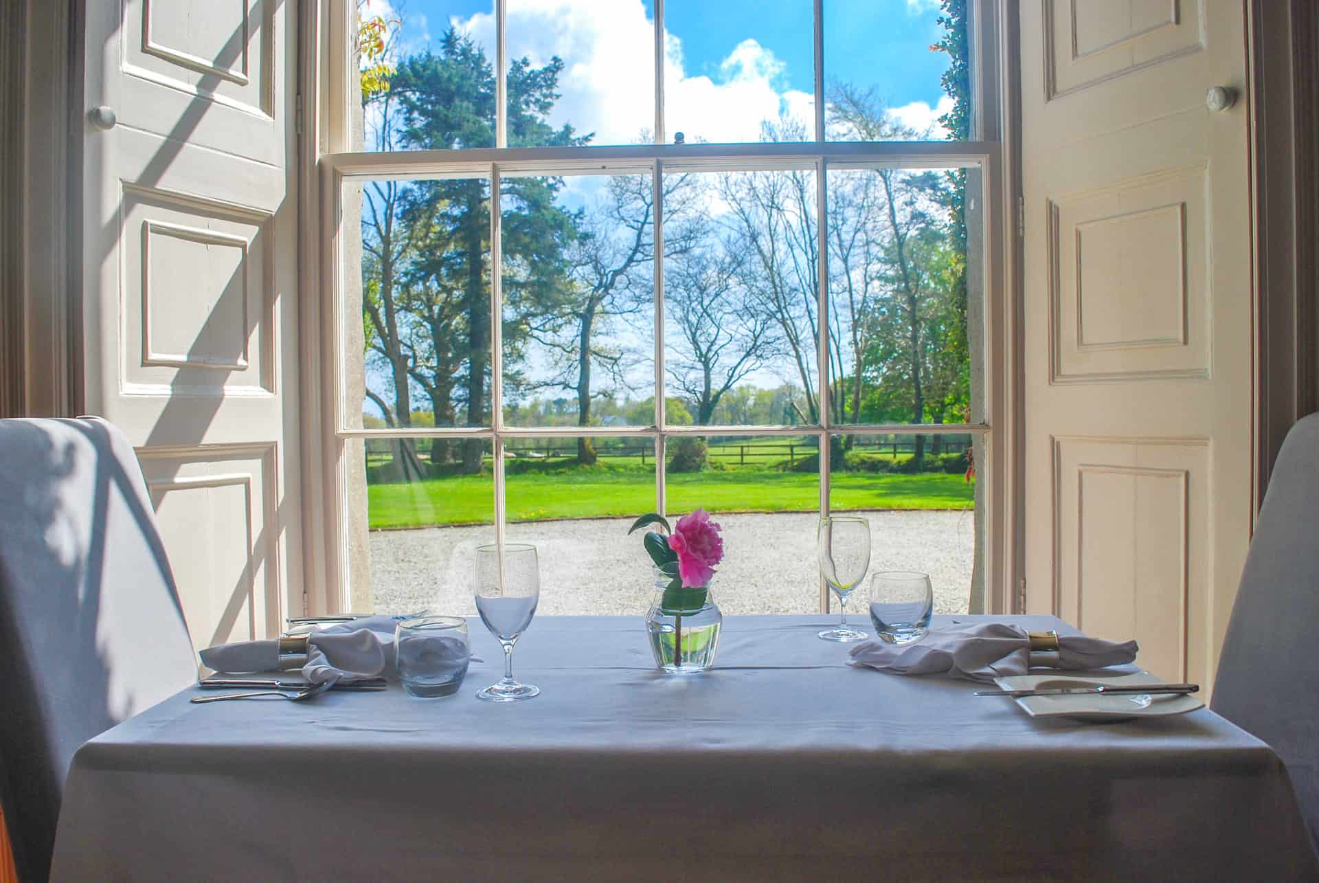 Elegant dining setup with a view of lush gardens through large windows.