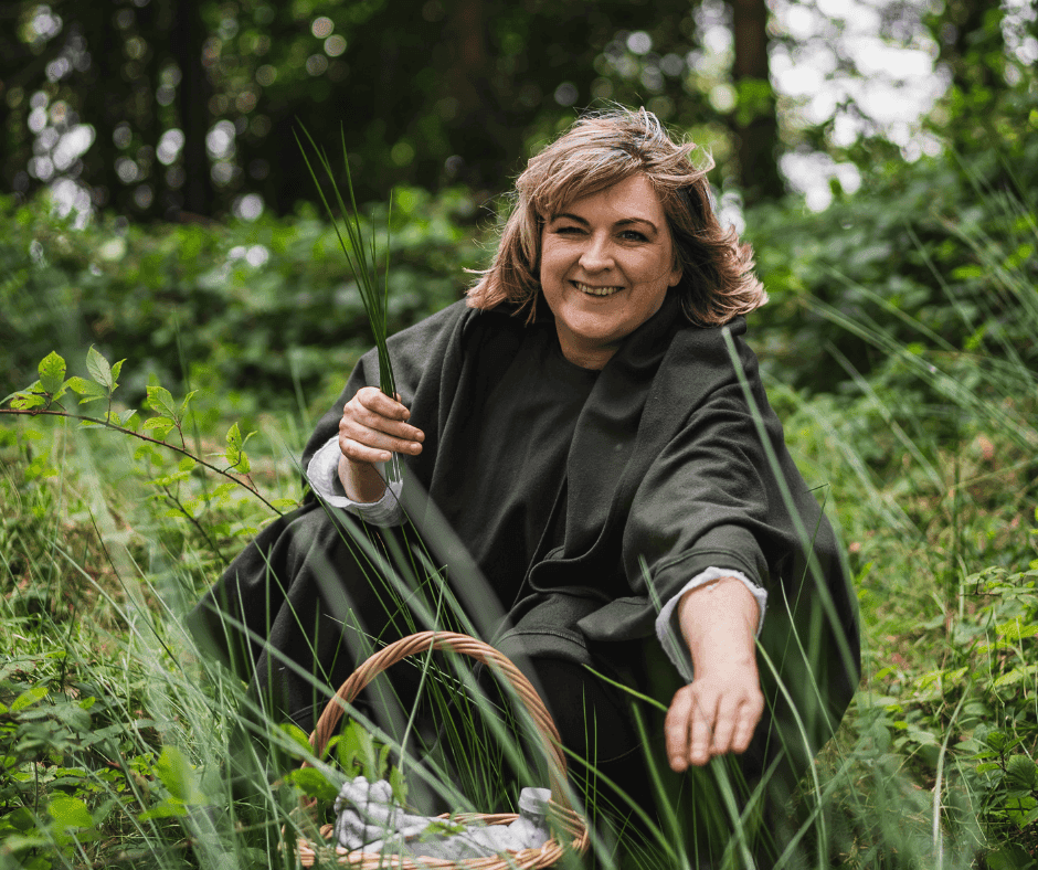 Woman harvesting herbs outdoors in a lush green forest setting.